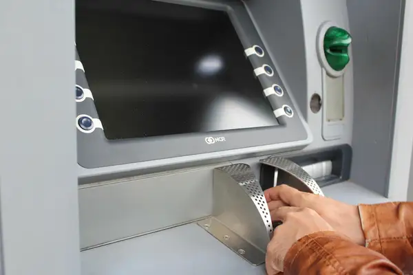 يد تسحب أوراقًا نقدية من صراف آلي، تمثيل لتحويل العملات الرقمية إلى ريالات سعودية